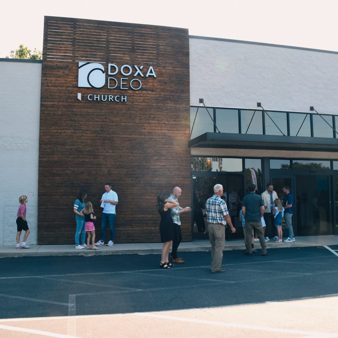 Doxa Deo church building with people in front of sign